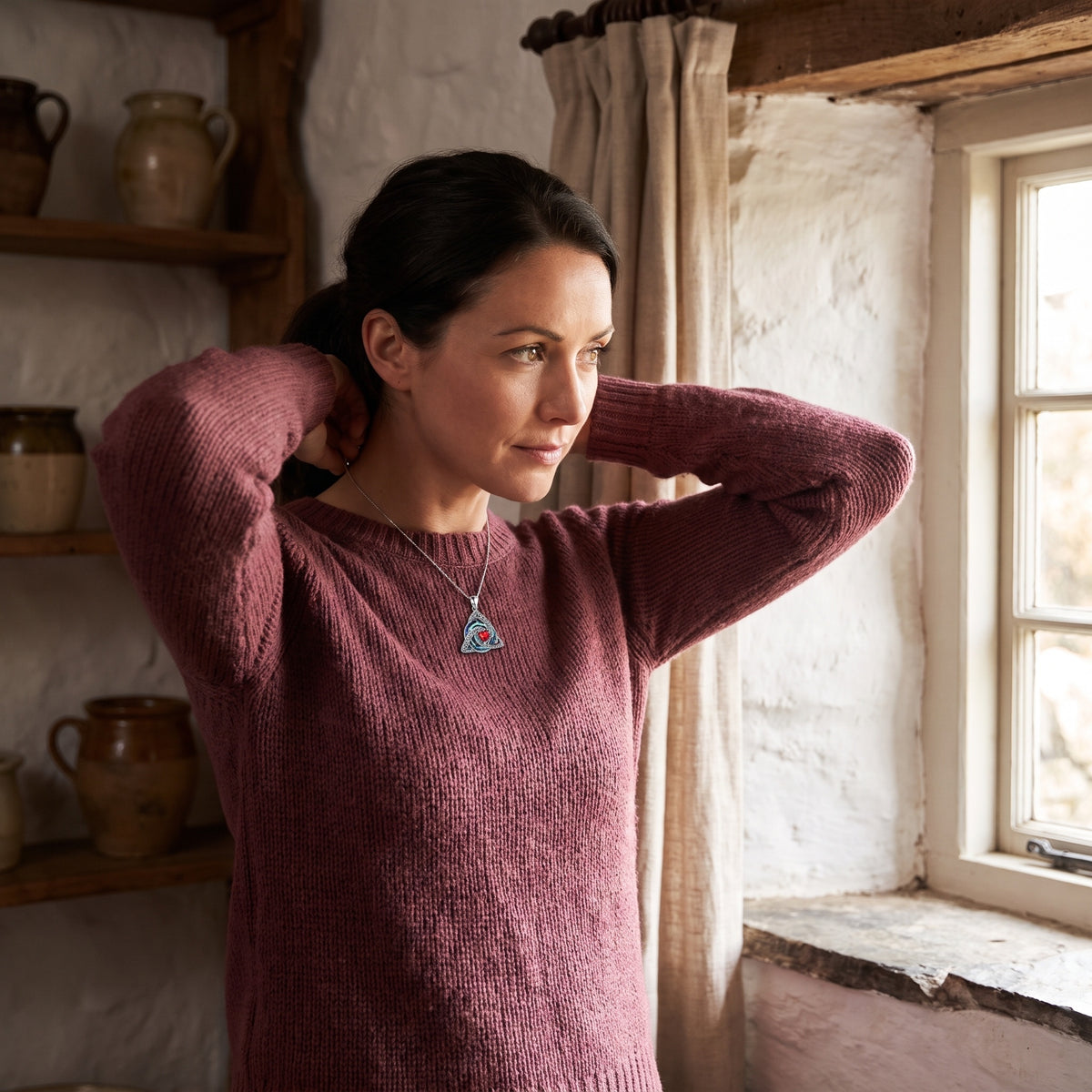 Woman fastening the witch knot necklace by a cottage window