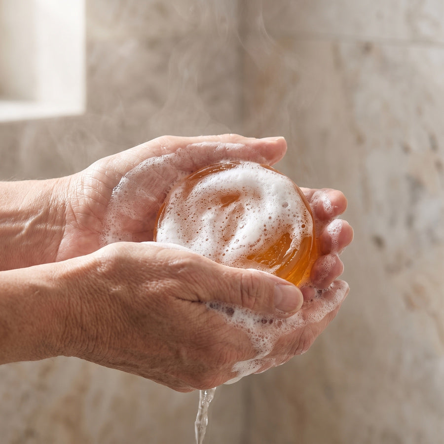 Hands working a rich lather from the Arausi bar in the shower